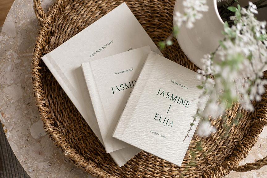 stack of stunning hand made wedding albums on a wicker tray and marble tabletop